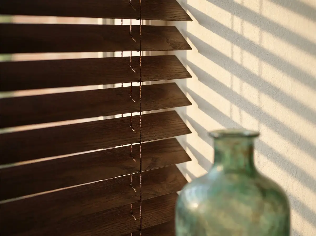 Close-up of dark timber venetian slats tilted to throw striped afternoon light across a plastered wall