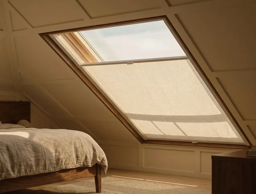Skylight blind fitted into the sloped frame of a roof window, held flat against the glass by side channels